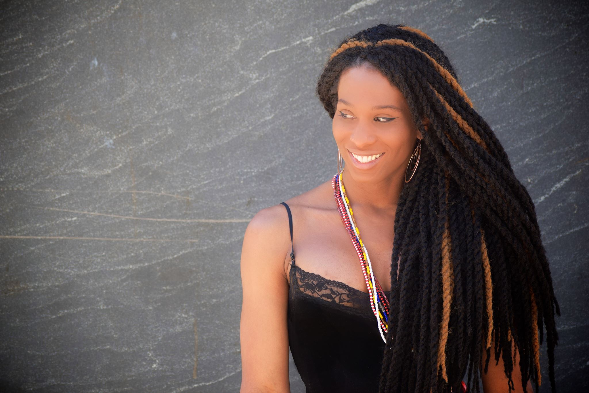 A Black woman with a black tank and long braids looks off to the side smiling.
