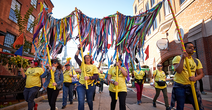 Staff of Long Wharf Theatre, dressed in yellow shirts and carrying an installation made of multi-colored ribbons, arrives on Audubon Street.