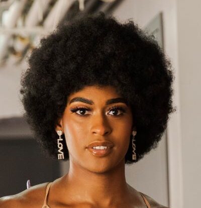 Mariyea is a Black Trans Woman depicted here with an Afro. Mariyea is 5’10 with dark brown eyes and hair and she is in her mid-20s.