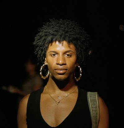 N’yomi Allure Stewart is a Black trans woman. In this photo, she wears gold jewelry and a black shirt and looks directly at the camera.